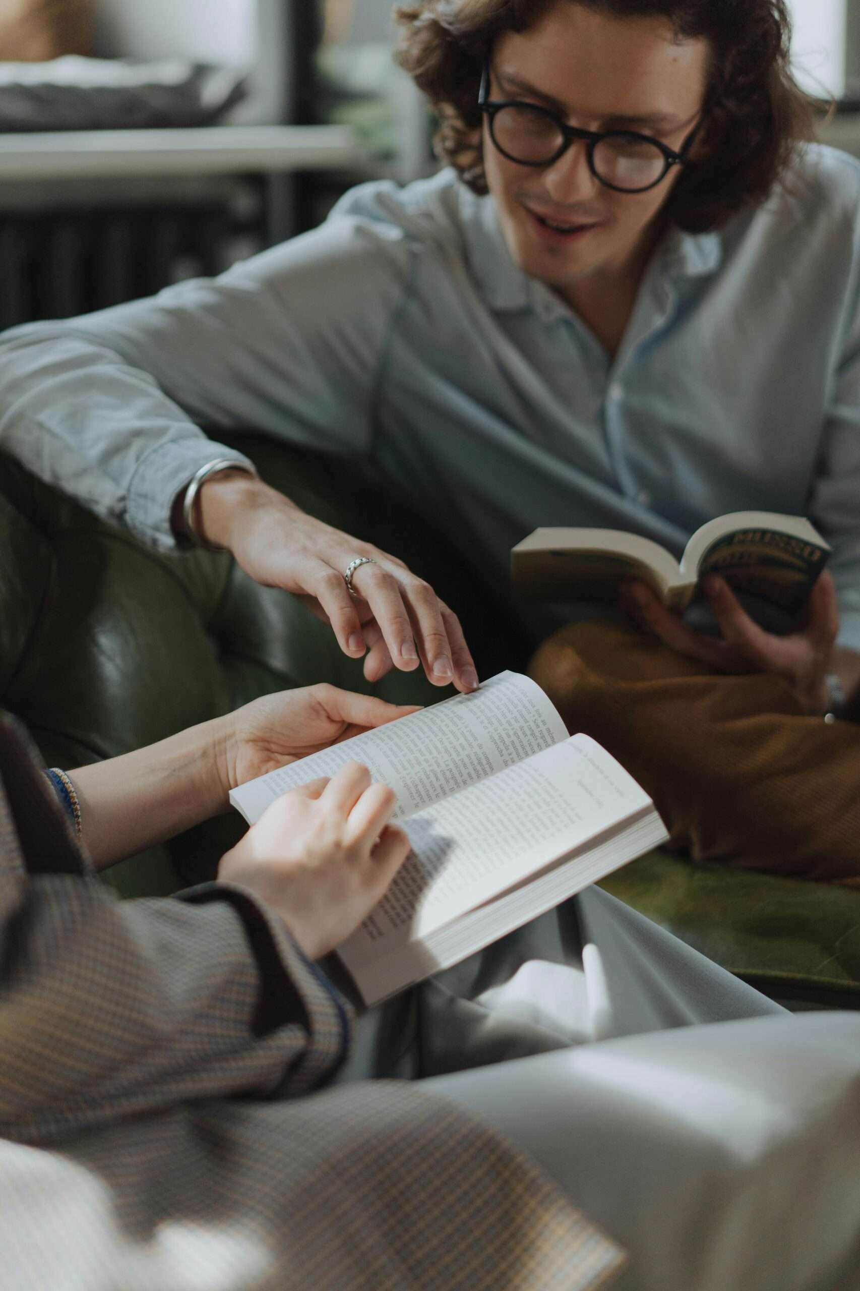 Two adults engaged in reading and discussing books on a comfortable sofa indoors.